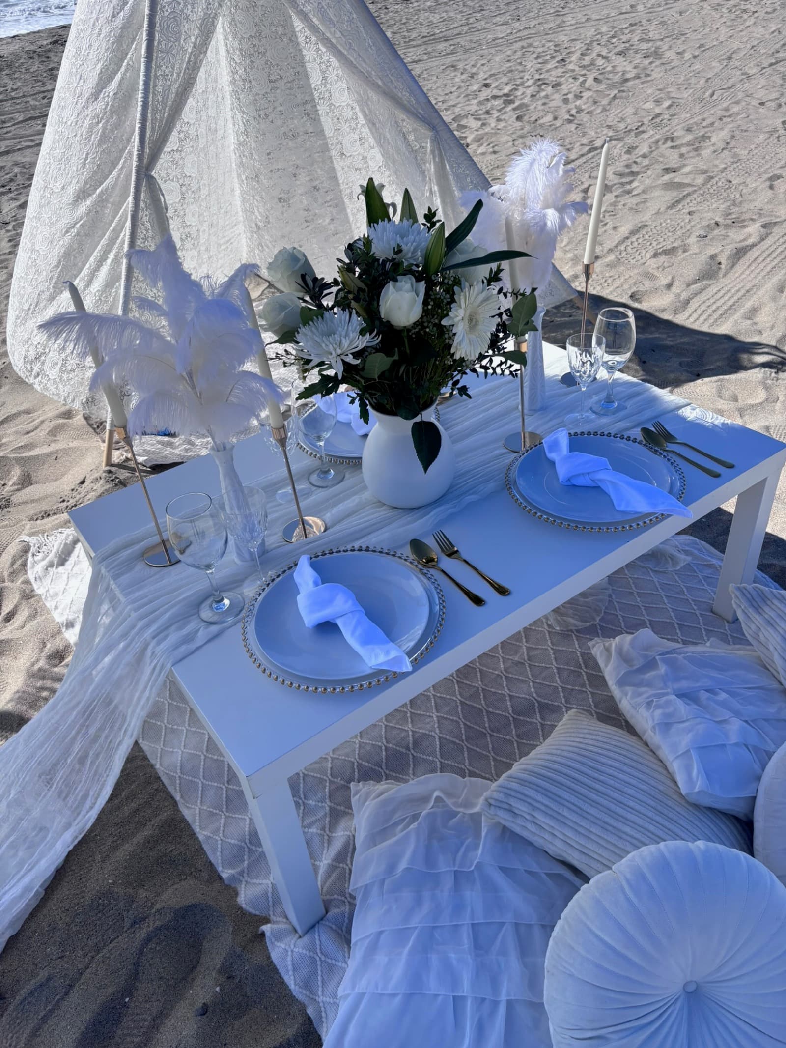 An elegant all-white beach tablescape with white ostrich-feather accents and a lace teepee