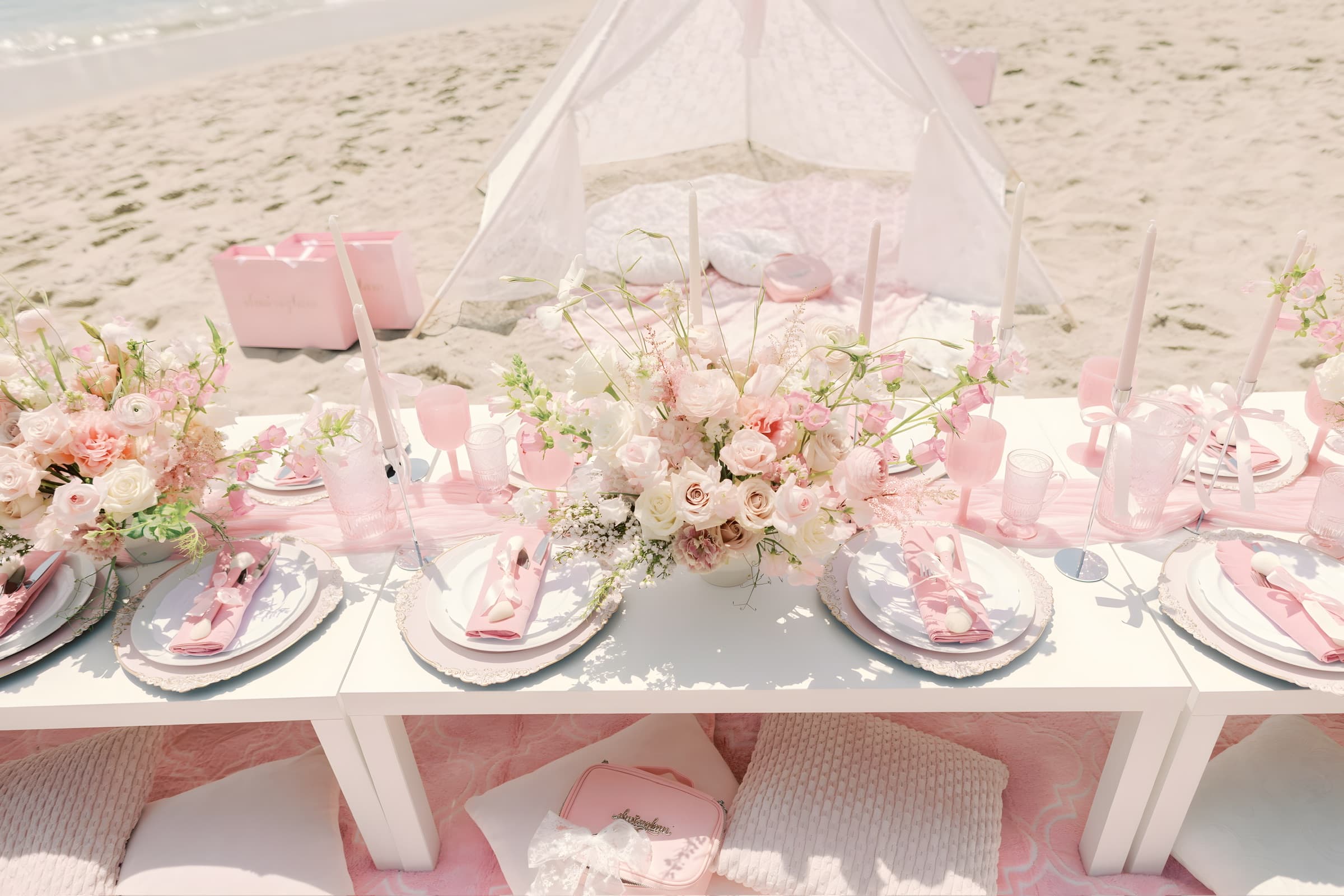 A wide pink cove table with a lace teepee and blush florals running toward turquoise surf