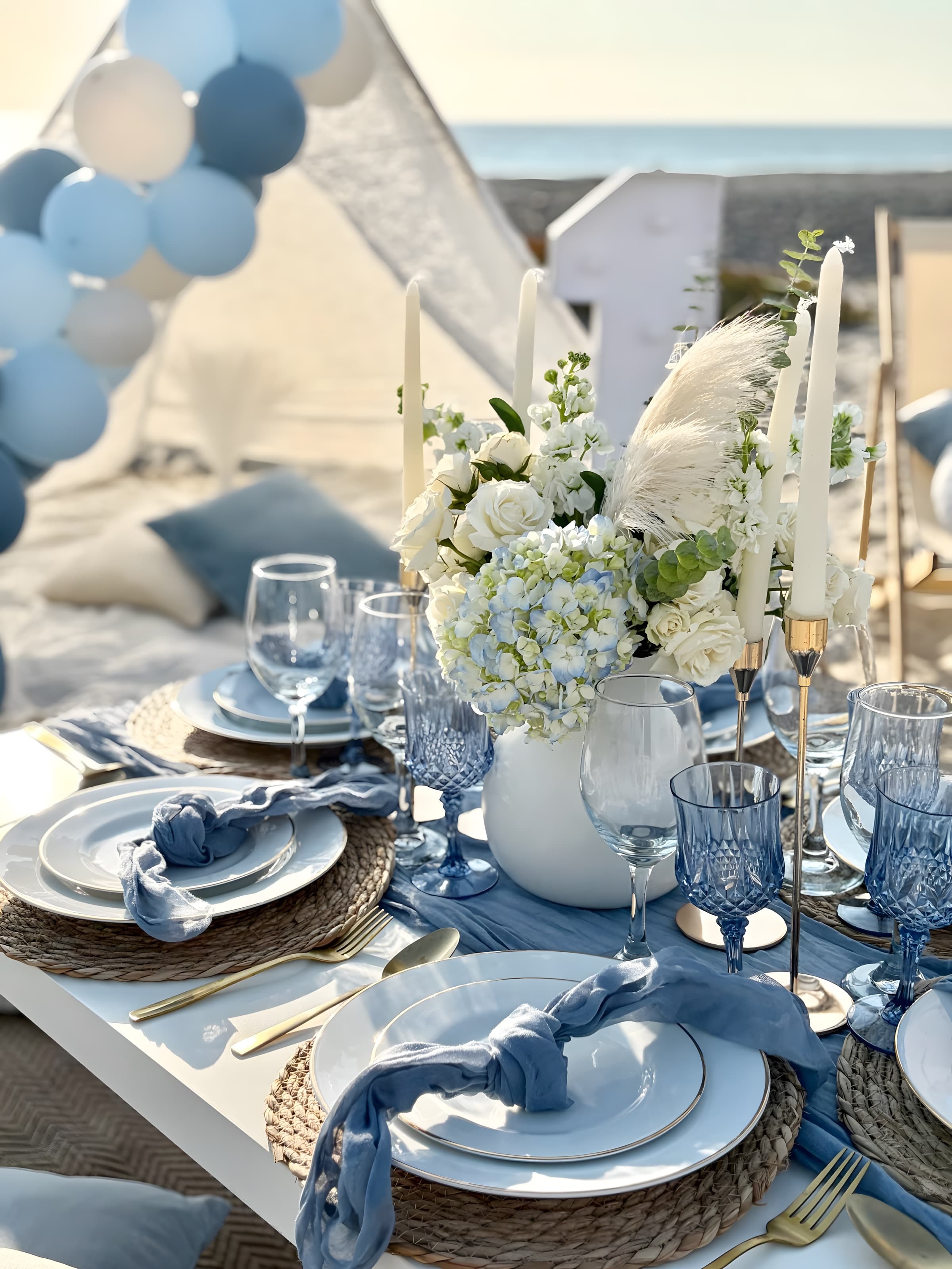 A dusty-blue centerpiece of white roses, hydrangea and pampas in a white vase amid blue goblets